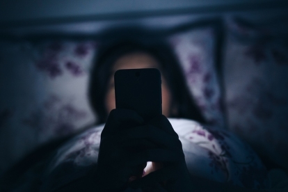 Frau liest und schreibt SMS auf dem Smartphone im Bett