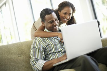 Привързана двойка, използваща лаптоп в хола