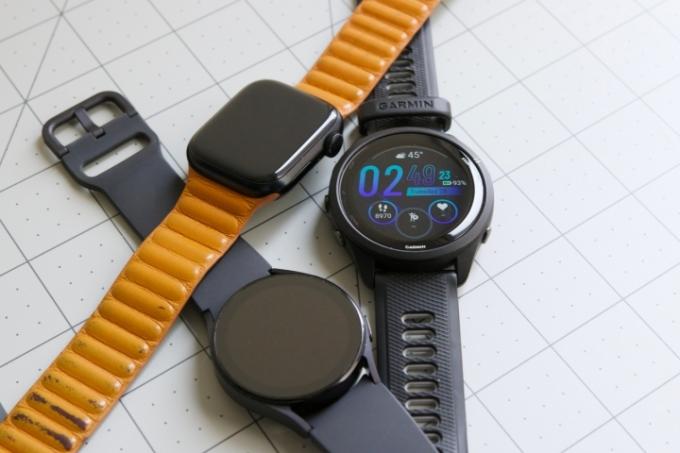 Apple Watch, Galaxy Watch 5 ו-Garmin Forerunner 265 שוכבים על שולחן אחד ליד השני.