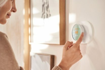 Mulher ajustando um termostato Wifi programável inteligente Google Nest. 