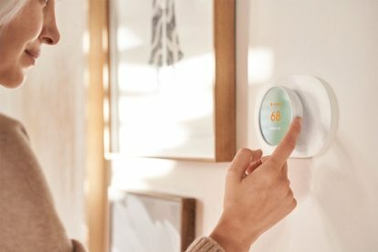 Nainen säätelemässä ohjelmoitavaa Google Nest Smart Wifi -termostaattia. 