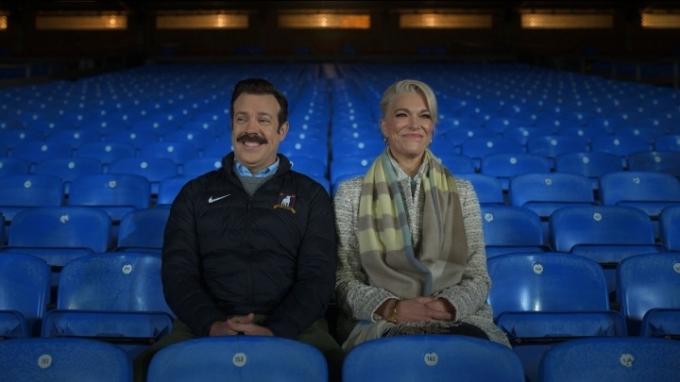Ted ja Rebecca istuvat stadionin istuimilla nauramassa yhdessä kohtauksessa Ted Lassosta.