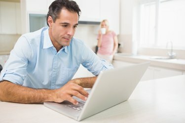 Bărbat care folosește un laptop cu o femeie care bea cafea la bucătărie