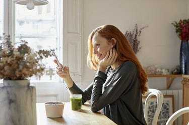 אישה מחייכת משתמשת בטלפון בזמן ארוחת בוקר