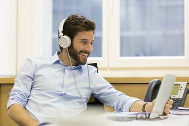 Veselý muž poslouchá hudbu a používá počítač v moderní kanceláři