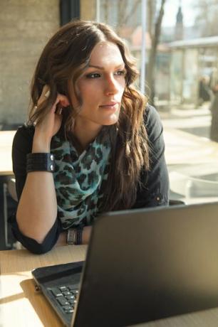 Piękna brunetka pracuje na laptopie w miejskiej kawiarni