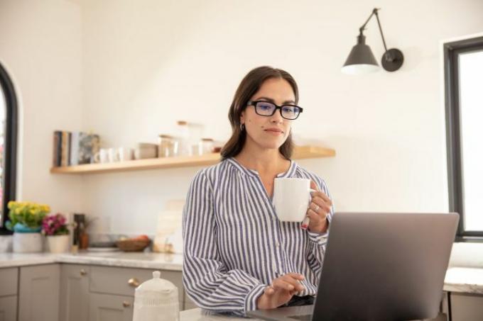 Una mujer con gafas de eco, sentada frente a su computadora, tomando café.