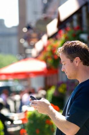 Muž pomocí mobilního PDA před letní pouliční kavárnou.