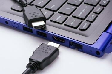 Du HDMI kabelio galai šalia modernaus mėlyno nešiojamojo kompiuterio HDMI prievado baltame fone