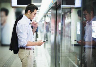 Verslininkas žiūri į savo telefoną ir laukia metro Pekine