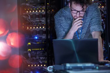 Koncentrēts IT tehniķis vīrietis, kas strādā pie klēpjdatora tumšā servera telpā