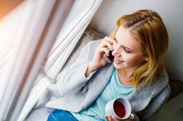 Frau auf der Fensterbank mit Smartphone beim Telefonieren