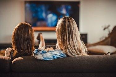 リビングルームのソファでリラックスし、テレビで映画を見ている2人の女性の背面図。