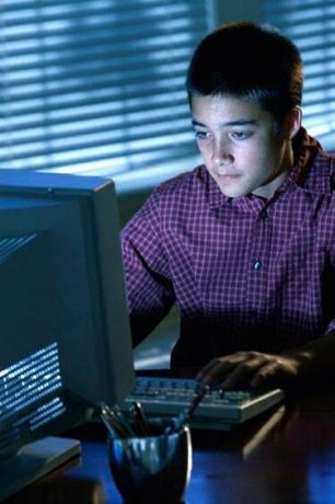 Nastoletni chłopiec siedzący przed monitorem komputera