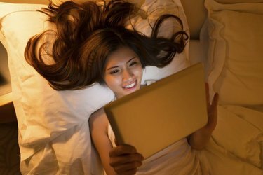 Fiatal nő használ valamilyen alkalmazást a digitális táblagépén éjjel, felülnézet