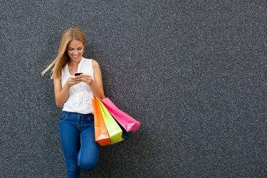 Jovem feliz digitando uma mensagem no telefone depois de fazer compras