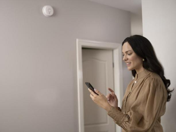 Mulher conectando-se ao alarme Wi-Fi Kidde Smoke + Monóxido de carbono com recursos inteligentes no telefone.