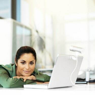 porträtt av en ung kvinna som lutar sig framåt på bordet med en bärbar dator framför sig