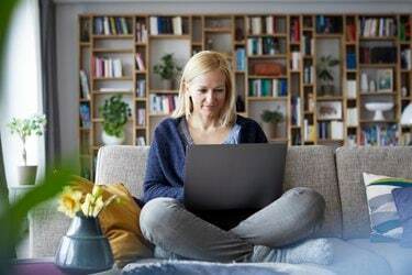 Wanita di rumah duduk di sofa menggunakan laptop