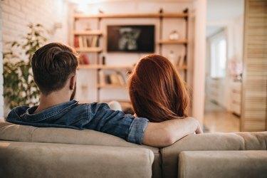 Vedere din spate a unui cuplu îndrăgostit care se uită la televizor acasă.