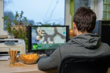მამაკაცი მოთამაშე, რომელიც თამაშობს სტრატეგიულ თამაშს კომპიუტერზე და ჭამს საჭმელს