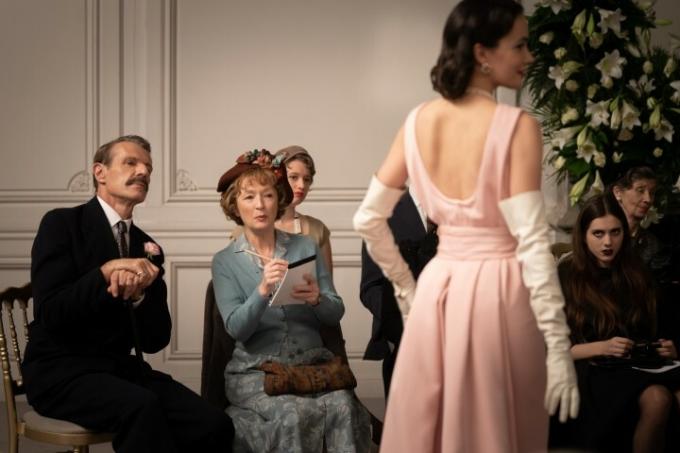 Људи гледају манекенку која позира у розе хаљини у Мрс. Харис одлази у Париз.