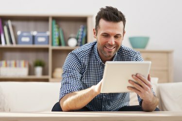 Usměvavý pohledný muž pomocí digitálního tabletu doma