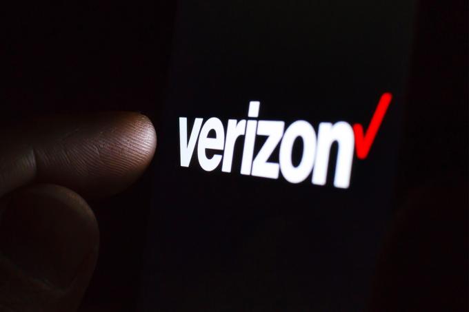 Logo Verizon pada layar ponsel pintar di ruangan gelap dan jari menyentuhnya.