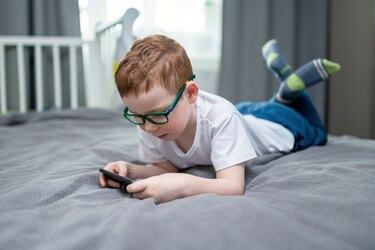 Schattige roodharige jongen die op het bed ligt en spelletjes speelt op smartphone