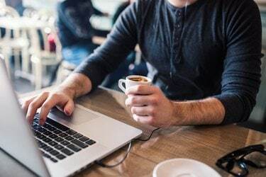 Mann hält Kaffee in einer Hand und arbeitet am Laptop