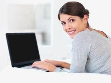 Mulher jovem sorrindo na cama com um laptop