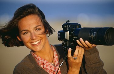 Жінка тримає камеру з телеоб'єктивом, посміхається, портрет