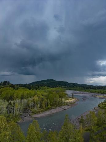 Ein Fluss mit einem dunklen Regensturm über einem Berg.