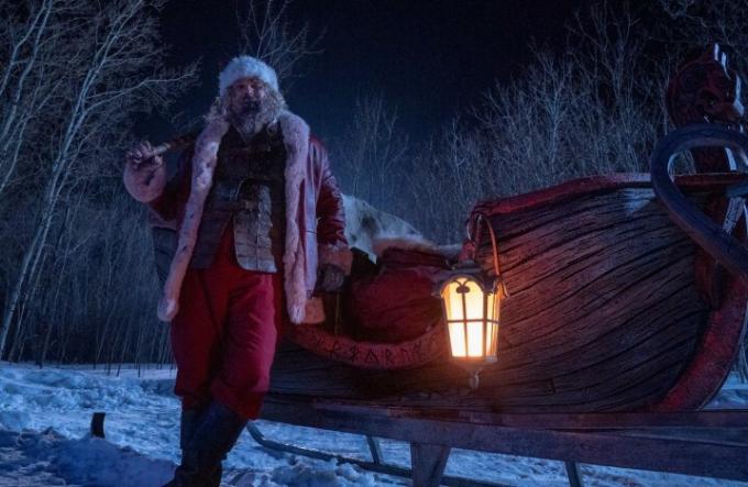 David Harbour, verkleed als kerstman, leunt tegen een slee.