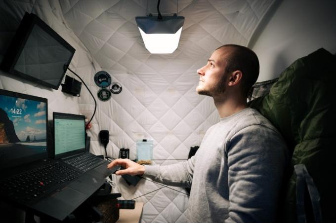Un hombre trabaja en una pequeña habitación con una luz circadiana en un entorno de luz diurna. 