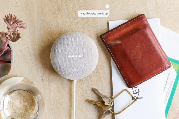 Googlen Nest Mini, valkoinen, pöydällä muiden henkilökohtaisten tavaroiden kanssa.