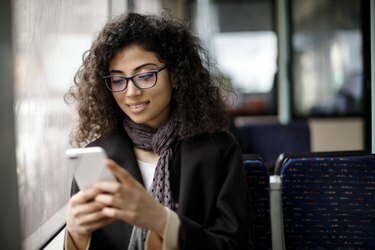 Leende ung kvinna som reser med buss och använder smart telefon