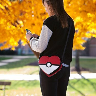 Moters nuotrauka, dėvinti širdies formos „Pokémon“ krepšį ir rašanti žinutes lauke.