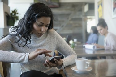 Donna che usa uno smartphone, beve caffè al bar