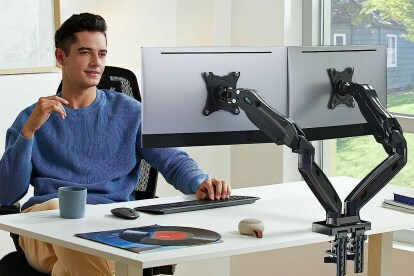Mann som bruker doble skjermarmer på skrivebordet sitt.