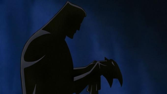 Stínová silueta Bruce Wayna oblékajícího Batmanův plášť.