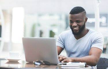 Uomo africano sorridente che invia messaggi di testo sul computer portatile al bar