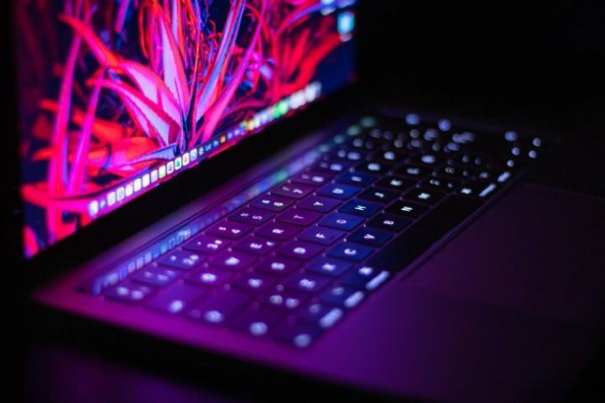 Zbliżenie na MacBooka oświetlonego neonami.