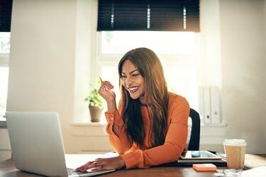 Hymyilevä nuori naisyrittäjä työskentelee kannettavalla tietokoneella kotona