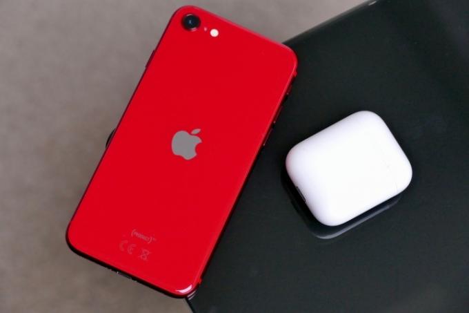 De iPhone SE 2020 in het rood op de hoek van een tafel naast een AirPods-hoesje.