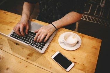 노트북을 사용하여 커피숍에 앉아 있는 젊은 남자