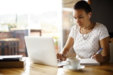 Mujer joven atractiva que trabaja en la computadora portátil y tomando notas en un café