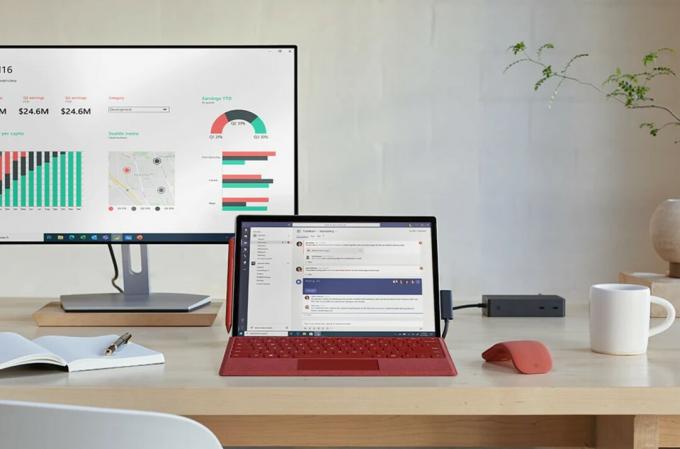 Microsoft Surface Pro 7+ di atas meja, dengan monitor di belakangnya.