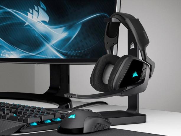 Corsair Void RGB Elite gaming hovedtelefoner på et stativ ved siden af ​​en gaming pc.