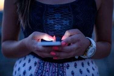 Sieviete raksta tālruņa ziņojumu sociālajā tīklā saulrietā